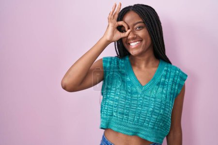 Photo for Young african american with braids standing over pink background doing ok gesture with hand smiling, eye looking through fingers with happy face. - Royalty Free Image