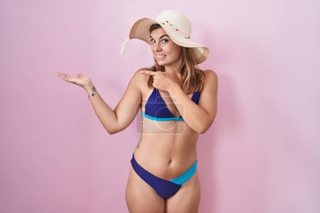 Foto de Mujer hispana joven vistiendo bikini sobre fondo rosa asombrada y sonriendo a la cámara mientras se presenta con la mano y señalando con el dedo. - Imagen libre de derechos