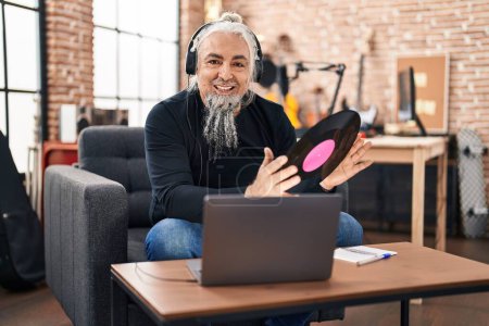 Photo for Middle age grey-haired man musician listening to music holding vinyl disc at music studio - Royalty Free Image
