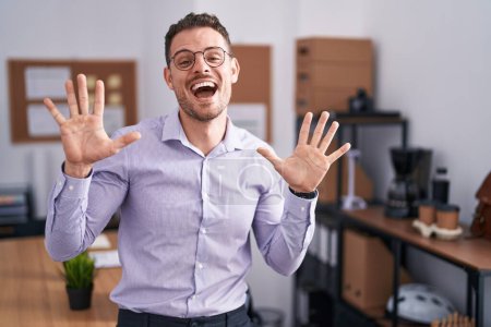 Foto de Joven hombre hispano en la oficina mostrando y señalando con los dedos el número diez mientras sonríe confiado y feliz. - Imagen libre de derechos