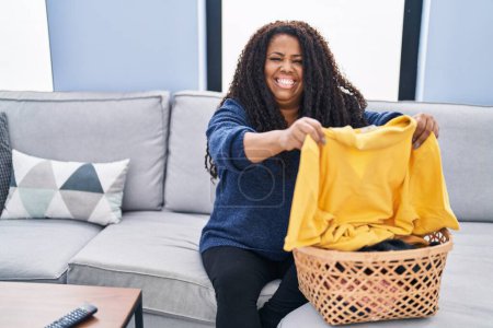 Téléchargez les photos : Afro-américaine femme assis sur canapé faire la lessive à la maison - en image libre de droit