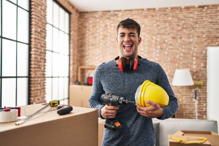 Téléchargez les photos : Jeune homme hispanique travaillant à la rénovation de la maison clin d'oeil en regardant la caméra avec une expression sexy, gai et heureux visage. - en image libre de droit