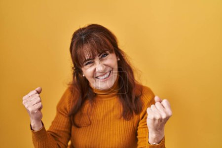 Téléchargez les photos : Femme hispanique du Moyen Âge debout sur fond jaune très heureux et excité de faire geste gagnant avec les bras levés, souriant et criant pour le succès. concept de célébration. - en image libre de droit