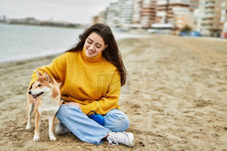 Téléchargez les photos : Belle jeune femme étreignant heureux shiba inu chien à la plage - en image libre de droit