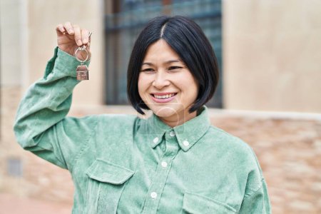 Téléchargez les photos : Jeune femme chinoise souriante confiante tenant la clé de la nouvelle maison à la rue - en image libre de droit