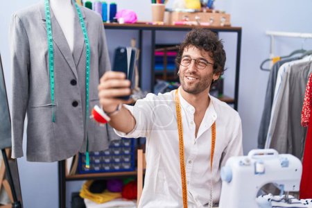 Foto de Young hispanic man tailor smiling confident make selfie by smartphone at clothing factory - Imagen libre de derechos