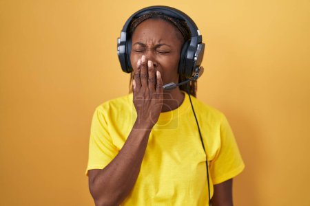 Téléchargez les photos : Femme afro-américaine écoutant de la musique à l'aide d'écouteurs ennuyés bâillant fatigué couvrant la bouche avec la main. agitation et somnolence. - en image libre de droit
