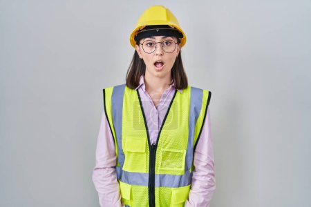 Foto de Hispanic girl wearing builder uniform and hardhat afraid and shocked with surprise expression, fear and excited face. - Imagen libre de derechos