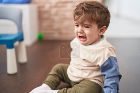 Foto de Adorable niño hispano sentado en el suelo llorando en casa - Imagen libre de derechos