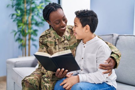 Foto de African american mother and son wearing soldier uniform reading book at home - Imagen libre de derechos