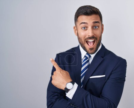 Photo for Handsome hispanic man wearing suit and tie with a big smile on face, pointing with hand finger to the side looking at the camera. - Royalty Free Image