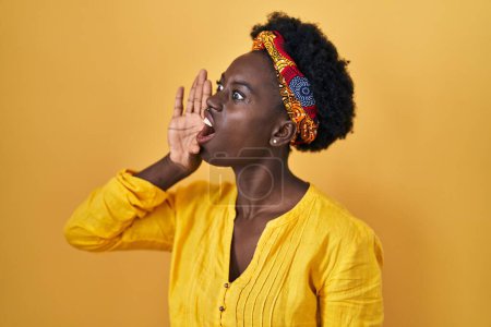 Foto de African young woman wearing african turban shouting and screaming loud to side with hand on mouth. communication concept. - Imagen libre de derechos