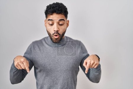 Téléchargez les photos : Hispanic man with beard standing over white background pointing down with fingers showing advertisement, surprised face and open mouth - en image libre de droit