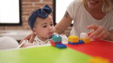 Téléchargez les photos : Femme et tout-petit jouant avec des blocs de construction assis sur la table à la maternelle - en image libre de droit