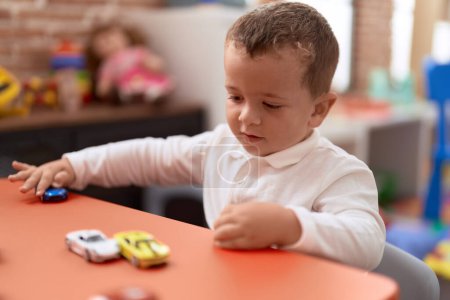 Foto de Adorable niño jugando con el juguete del coche sentado en la mesa en el jardín de infantes - Imagen libre de derechos