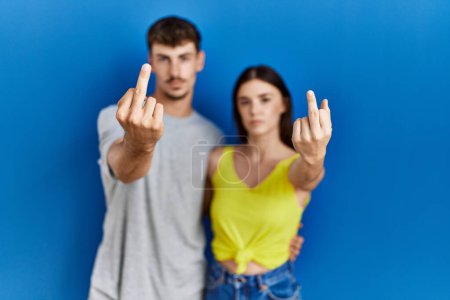 Foto de Young hispanic couple standing together over blue background showing middle finger, impolite and rude fuck off expression - Imagen libre de derechos