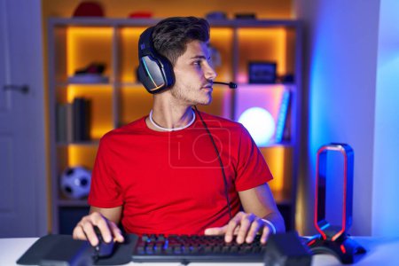 Foto de Young hispanic man playing video games looking to side, relax profile pose with natural face with confident smile. - Imagen libre de derechos