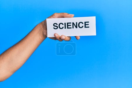 Téléchargez les photos : Hand of caucasian man holding paper with science word over isolated blue background - en image libre de droit