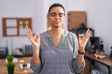 Photo for African american woman working at the office wearing glasses relax and smiling with eyes closed doing meditation gesture with fingers. yoga concept. - Royalty Free Image