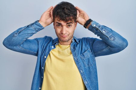 Téléchargez les photos : Young hispanic man standing over blue background doing bunny ears gesture with hands palms looking cynical and skeptical. easter rabbit concept. - en image libre de droit