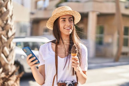 Téléchargez les photos : Young hispanic woman tourist using smartphone eating ice cream at street - en image libre de droit