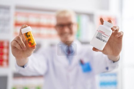 Foto de Joven hombre caucásico farmacéutico sosteniendo pastillas botellas en la farmacia - Imagen libre de derechos