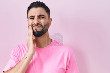 Foto de Joven hispano de pie sobre fondo rosa tocando boca con mano con expresión dolorosa debido a dolor de muelas o enfermedad dental en los dientes. dentista - Imagen libre de derechos