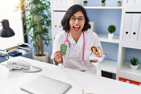 Photo for Young hispanic doctor woman holding anatomical model of uterus with fetus and birth control pills smiling and laughing hard out loud because funny crazy joke. - Royalty Free Image