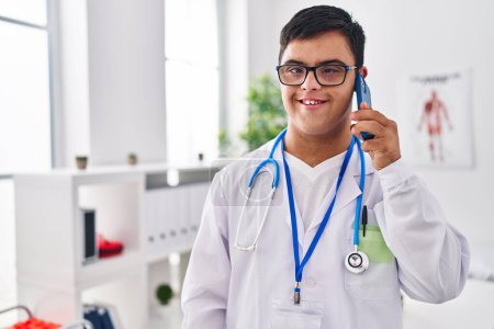Téléchargez les photos : Homme trisomique portant l'uniforme de médecin parlant sur le smartphone à la clinique - en image libre de droit