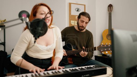 Photo for Man and woman singing son playing guitar and keyboard piano at music studio - Royalty Free Image