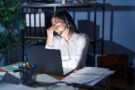 Photo for Young brunette woman wearing call center agent headset working late at night tired rubbing nose and eyes feeling fatigue and headache. stress and frustration concept. - Royalty Free Image