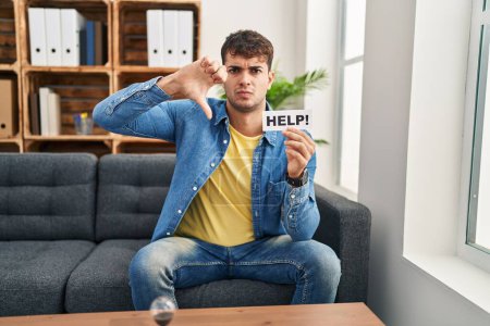 Téléchargez les photos : Young hispanic man at therapy asking for help with angry face, negative sign showing dislike with thumbs down, rejection concept - en image libre de droit