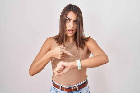 Foto de Young hispanic woman standing over white background in hurry pointing to watch time, impatience, upset and angry for deadline delay - Imagen libre de derechos