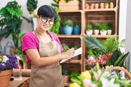 Photo for Middle age chinese woman florist smiling confident writing on notebook at flower shop - Royalty Free Image