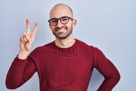 Photo for Young bald man with beard standing over white background wearing glasses smiling looking to the camera showing fingers doing victory sign. number two. - Royalty Free Image