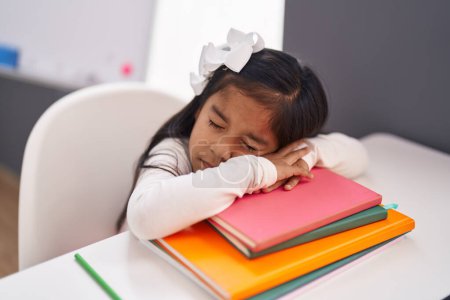 Foto de Adorable estudiante hispana apoyada en libro durmiendo en el aula - Imagen libre de derechos