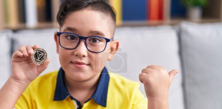 Foto de Young hispanic kid holding tron cryptocurrency coin pointing thumb up to the side smiling happy with open mouth - Imagen libre de derechos