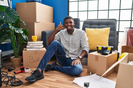 Photo for African american man sitting on the floor at new home smiling doing phone gesture with hand and fingers like talking on the telephone. communicating concepts. - Royalty Free Image