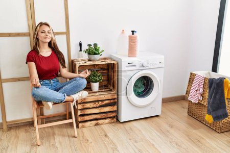 Téléchargez les photos : Young caucasian girl doing yoga waiting for washing machine at home. - en image libre de droit