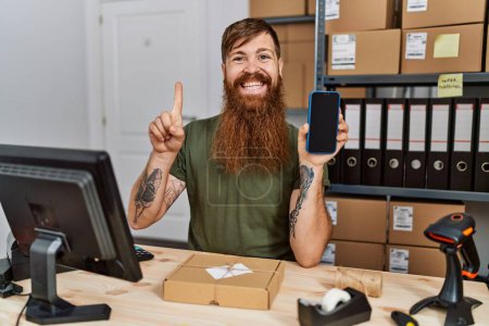 Téléchargez les photos : Homme rousse à longue barbe travaillant dans une petite entreprise tenant smartphone souriant avec une idée ou une question pointant du doigt avec un visage heureux, numéro un - en image libre de droit
