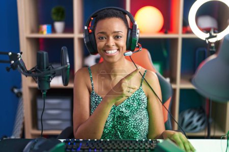 Foto de Mujer afroamericana jugando videojuegos sonriendo feliz apuntando con la mano y el dedo hacia un lado - Imagen libre de derechos