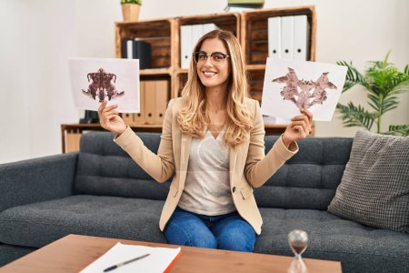Foto de Young blonde therapist woman holding rorschach test smiling with a happy and cool smile on face. showing teeth. - Imagen libre de derechos