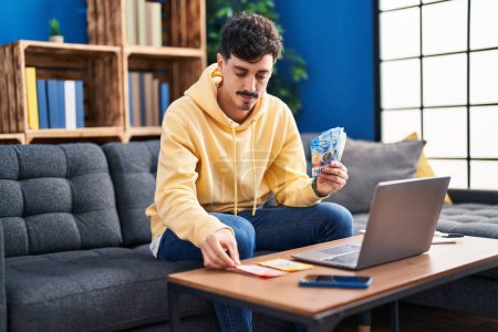 Téléchargez les photos : Jeune homme caucasien utilisant un ordinateur portable comptant les billets en francs suisses à la maison - en image libre de droit