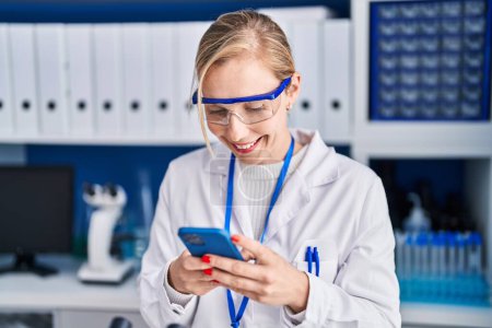 Photo for Young blonde woman scientist smiling confident using smartphone at laboratory - Royalty Free Image