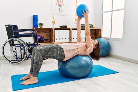 Photo for Middle age hispanic woman training with pilates ball at physiotherapy clinic - Royalty Free Image
