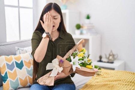 Photo for Chinese young woman holding bouquet of white flowers yawning tired covering half face, eye and mouth with hand. face hurts in pain. - Royalty Free Image