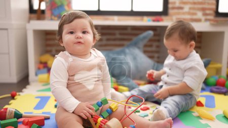 Foto de Dos niños pequeños jugando con juguetes sentados en el suelo en el jardín de infantes - Imagen libre de derechos