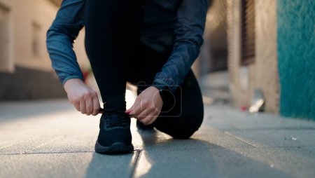 Foto de Joven pelirroja con ropa deportiva atando zapatos en la calle - Imagen libre de derechos