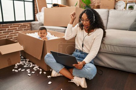 Téléchargez les photos : Young hispanic mother and kid sitting on the floor at new home using laptop screaming proud, celebrating victory and success very excited with raised arm - en image libre de droit