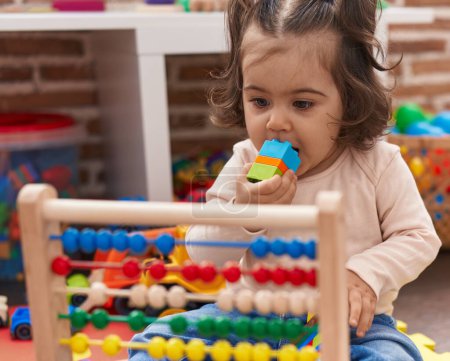 Foto de Adorable chica hispana jugando con ábaco chupando bloques de construcción en el jardín de infantes - Imagen libre de derechos